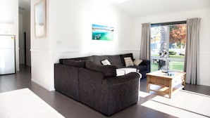 A modern living room with a sectional sofa, a wooden coffee table, and a large window with curtains. - BIG4 Batemans Bay Beach Resort (Batehaven)