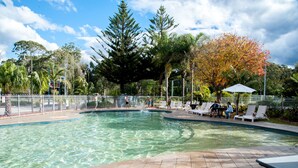 A swimming pool with a tiled deck, surrounded by a fence, and trees in the background. - BIG4 Batemans Bay Beach Resort (Batehaven)