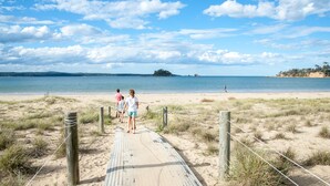 A sandy beach with a wooden boardwalk leading to the water, surrounded by grass and a clear sky. - BIG4 Batemans Bay Beach Resort (Batehaven)