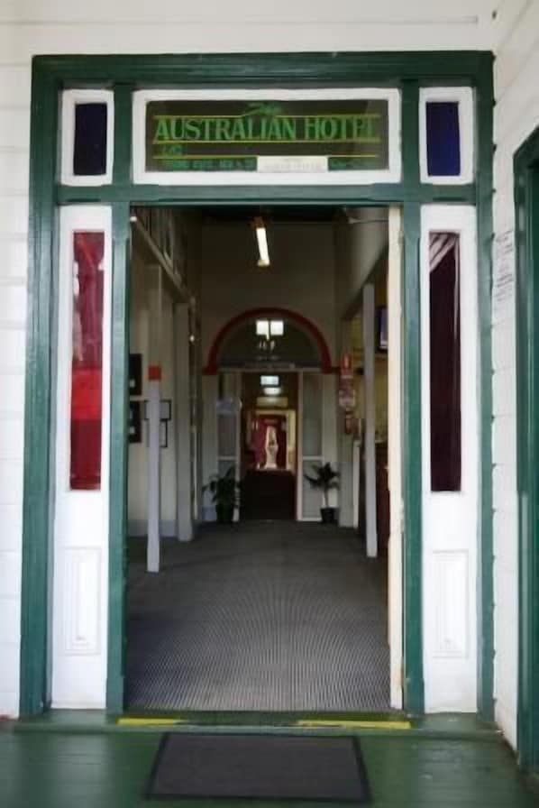 La entrada al Hotel Australiano, con fachada verde y blanca, piso de baldosas y un arco central.