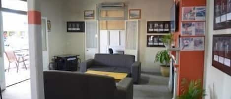 Een kamer met een bank, een tafeltje, een bloempot en een muur met ingelijste foto's.