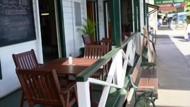 An outdoor seating area with wooden tables and chairs, a green railing, and a chalkboard with writing. - Australian Hotel Boonah (Boonah)