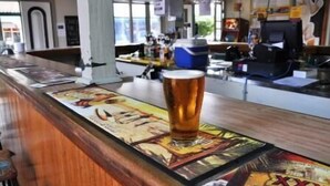 A bar area with a glass of beer on a coaster, a poster with a cartoon character, and a counter with various items. - Australian Hotel Boonah (Boonah)