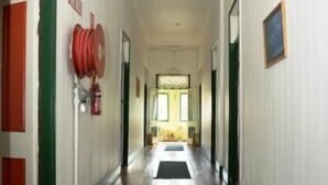 A long, narrow hallway with wooden floors and white walls, leading to a room with a window. - Australian Hotel Boonah (Boonah)