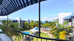 A balcony with a view of a resort area, including palm trees and a pool.