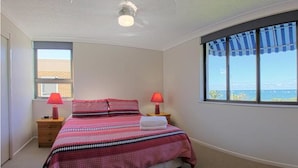 A bedroom with a large window, a bed with a striped bedspread, two bedside lamps, and a view of the sea.