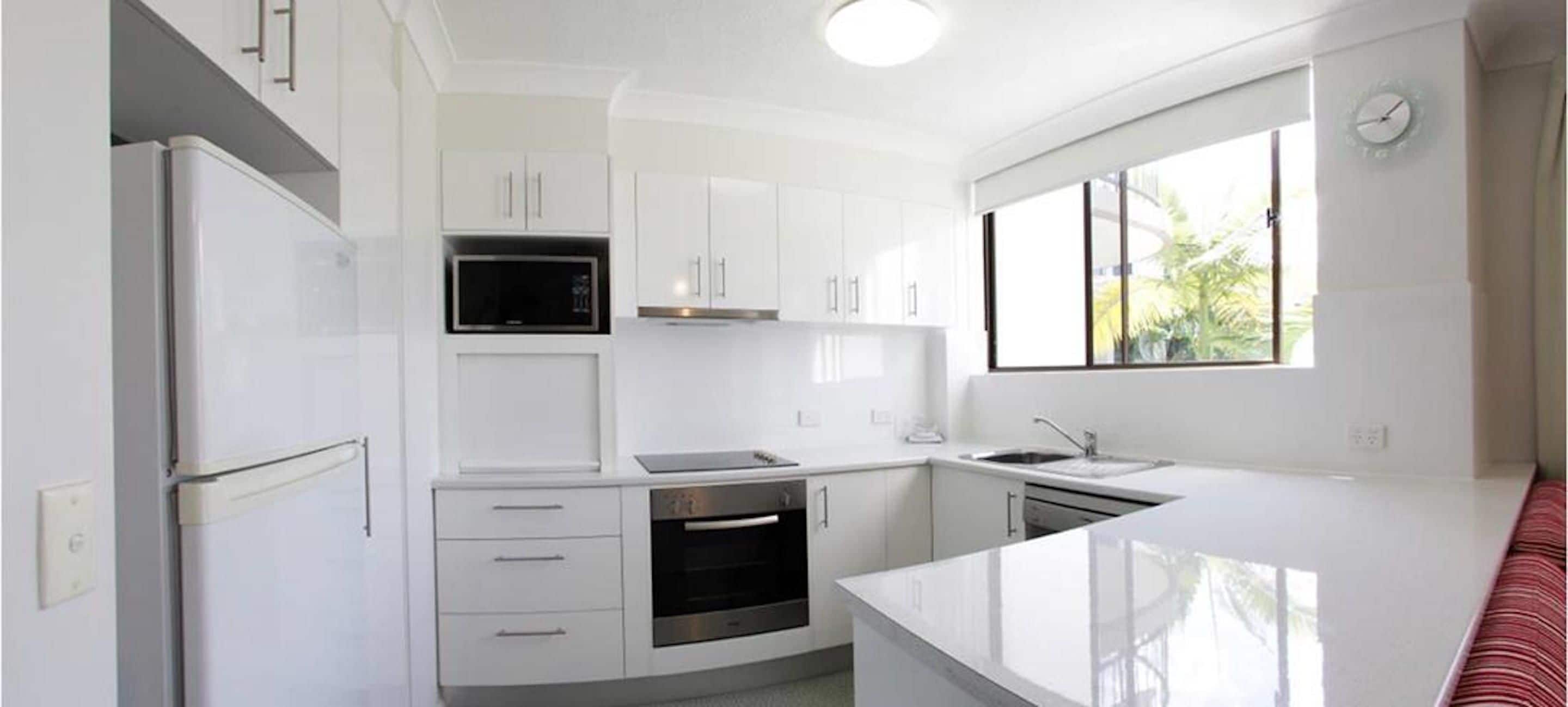 A modern kitchen with white cabinetry, a built-in oven, a microwave, and a sink.