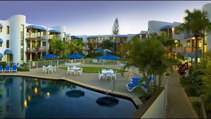 A hotel with a swimming pool, outdoor seating, and multiple balconies with umbrellas.