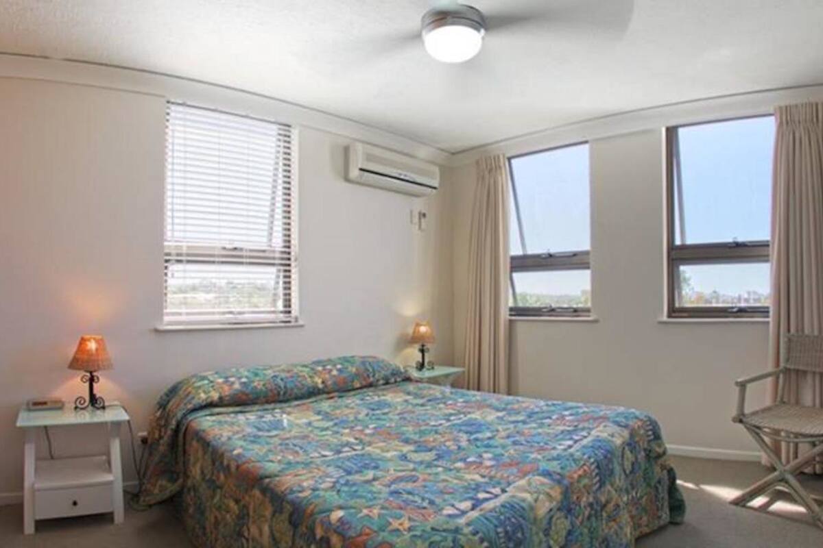 Un dormitorio con dos camas, una silla, una mesita de noche con lámpara y una ventana con vistas.
