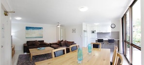 Een moderne woonkamer met een bank, een houten eettafel en een keuken op de achtergrond.