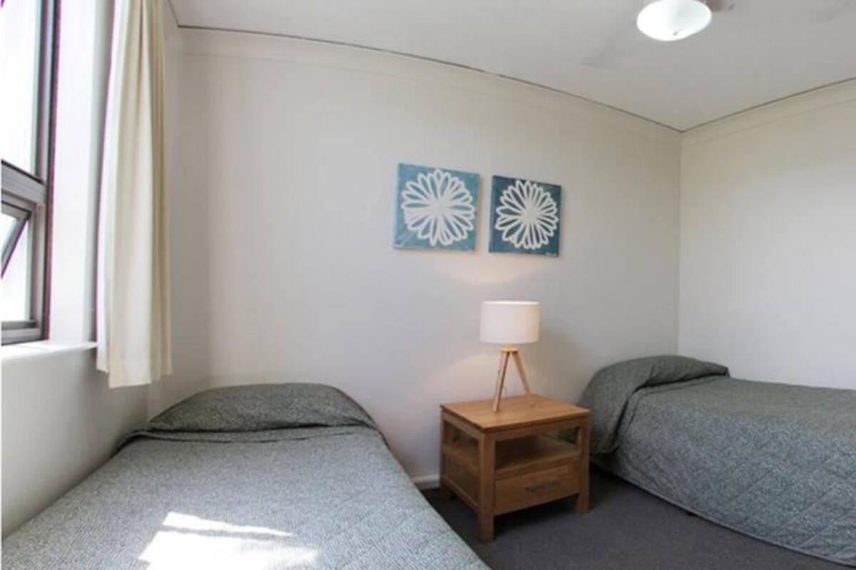 Una habitación pequeña y sencilla con dos camas individuales, una mesita de noche con lámpara y dos adornos en la pared.