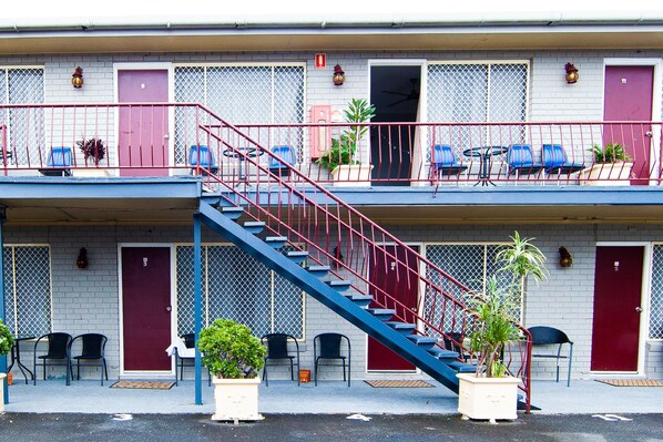 A motel with a red and blue exterior, a staircase, and outdoor seating with chairs and tables.