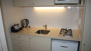 A compact kitchen with a stainless steel sink, a microwave, a gas stove, and a small refrigerator. - Methven Motels & Apartments (Methven)
