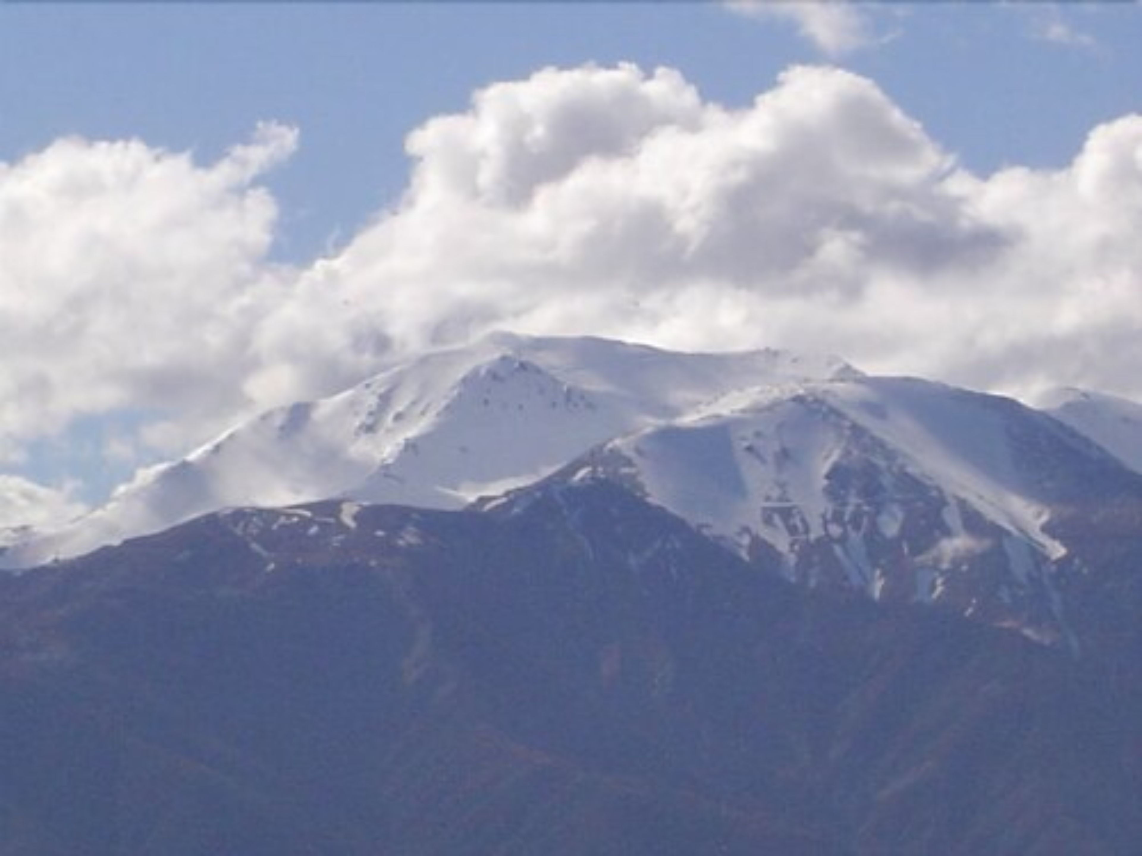 A snow-covered mountain with a clear sky and clouds.