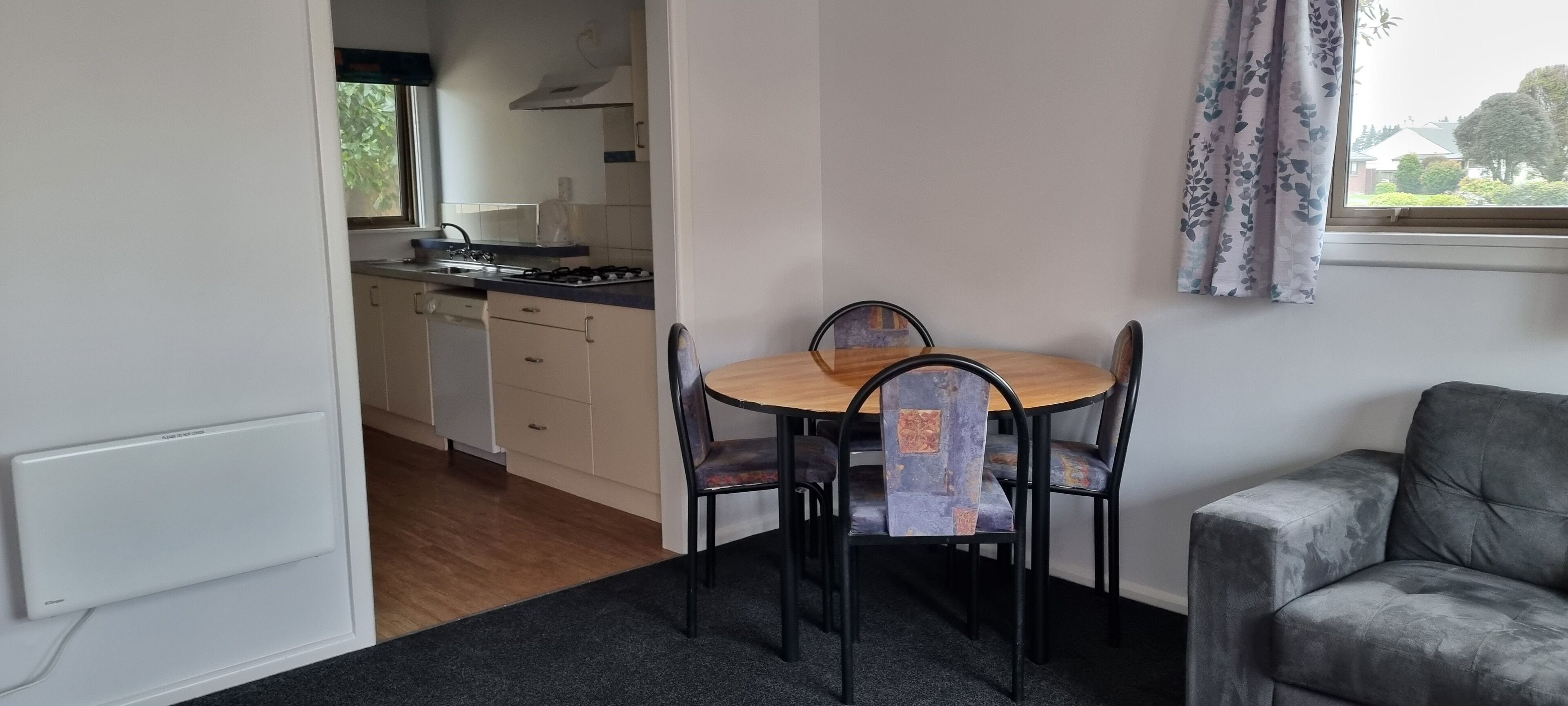 Une cuisine compacte avec un coin repas comprenant une table et des chaises, un canapé et une fenêtre avec des rideaux.