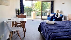 A hotel room with a bed, a desk, a chair, and a balcony with a view of greenery. - Methven Motels & Apartments (Methven)