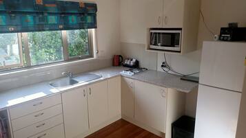 Una cocina con ventana, pileta, microondas y placares.