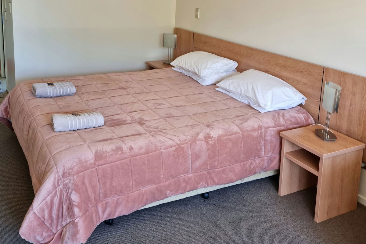 Habitación de hotel con una cama tamaño queen, dos mesitas de noche y un cabecero.