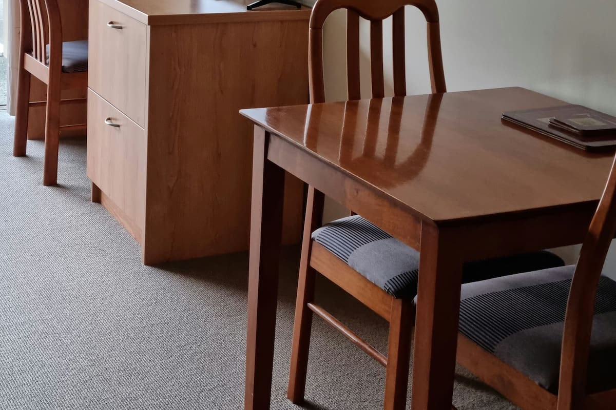 Un escritorio de madera con un monitor de computadora, dos sillas y una pequeña mesa con una libreta.
