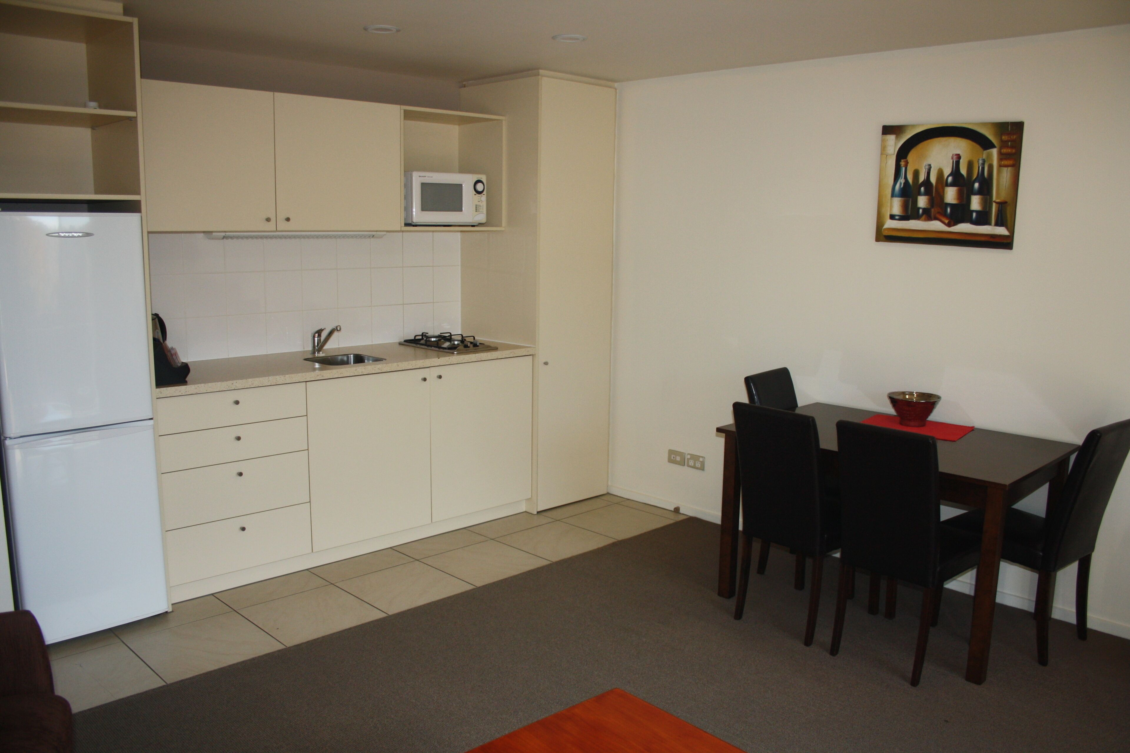 Una cocina compacta con microondas, estufa y refrigerador. Hay una mesa de comedor con sillas y un cuadro en la pared.