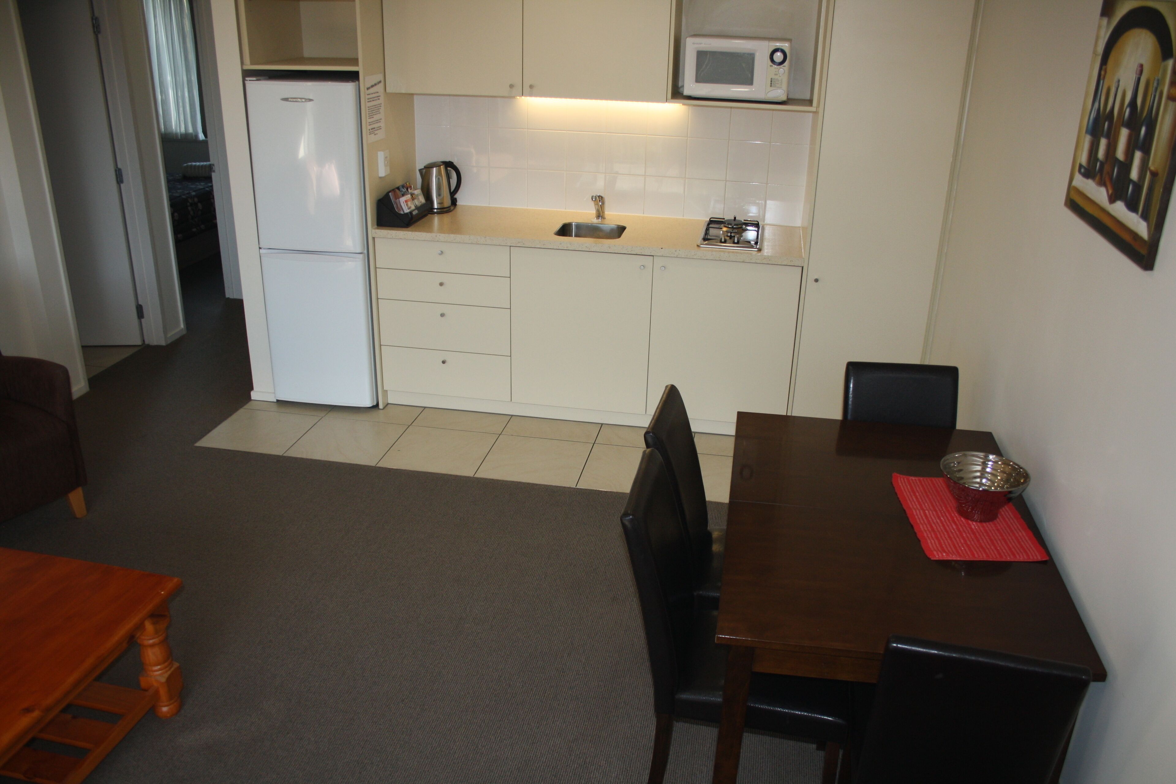 Una cocina compacta con refrigerador, microondas, pileta y comedor con mesa y sillas.