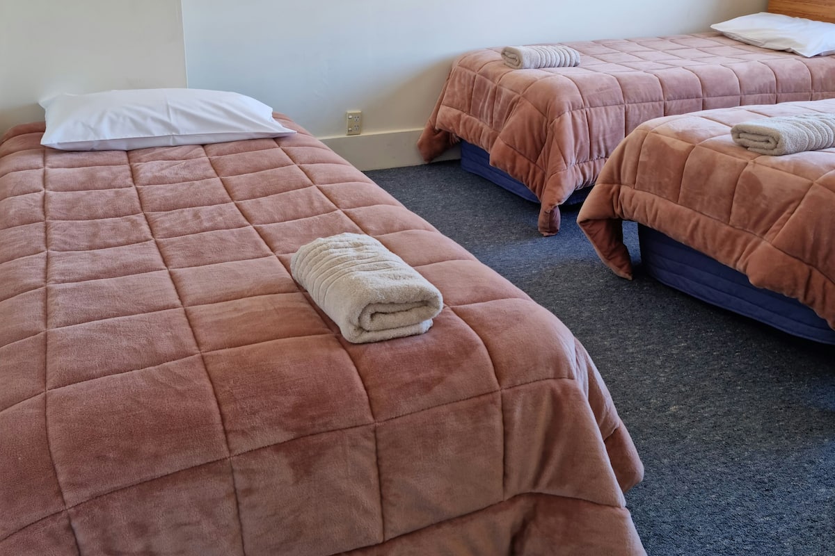 Habitación de hotel con dos camas, cada una con una colcha acolchada rosa y una toalla enrollada encima.