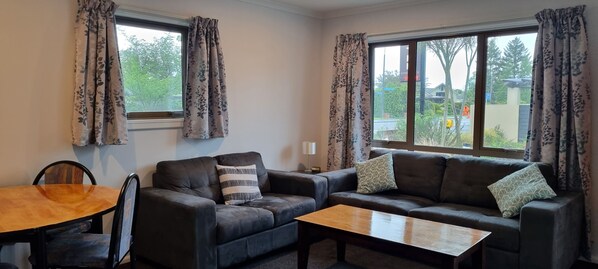 A living room with a sofa, a coffee table, and a dining table. - Methven Motels & Apartments (Methven)