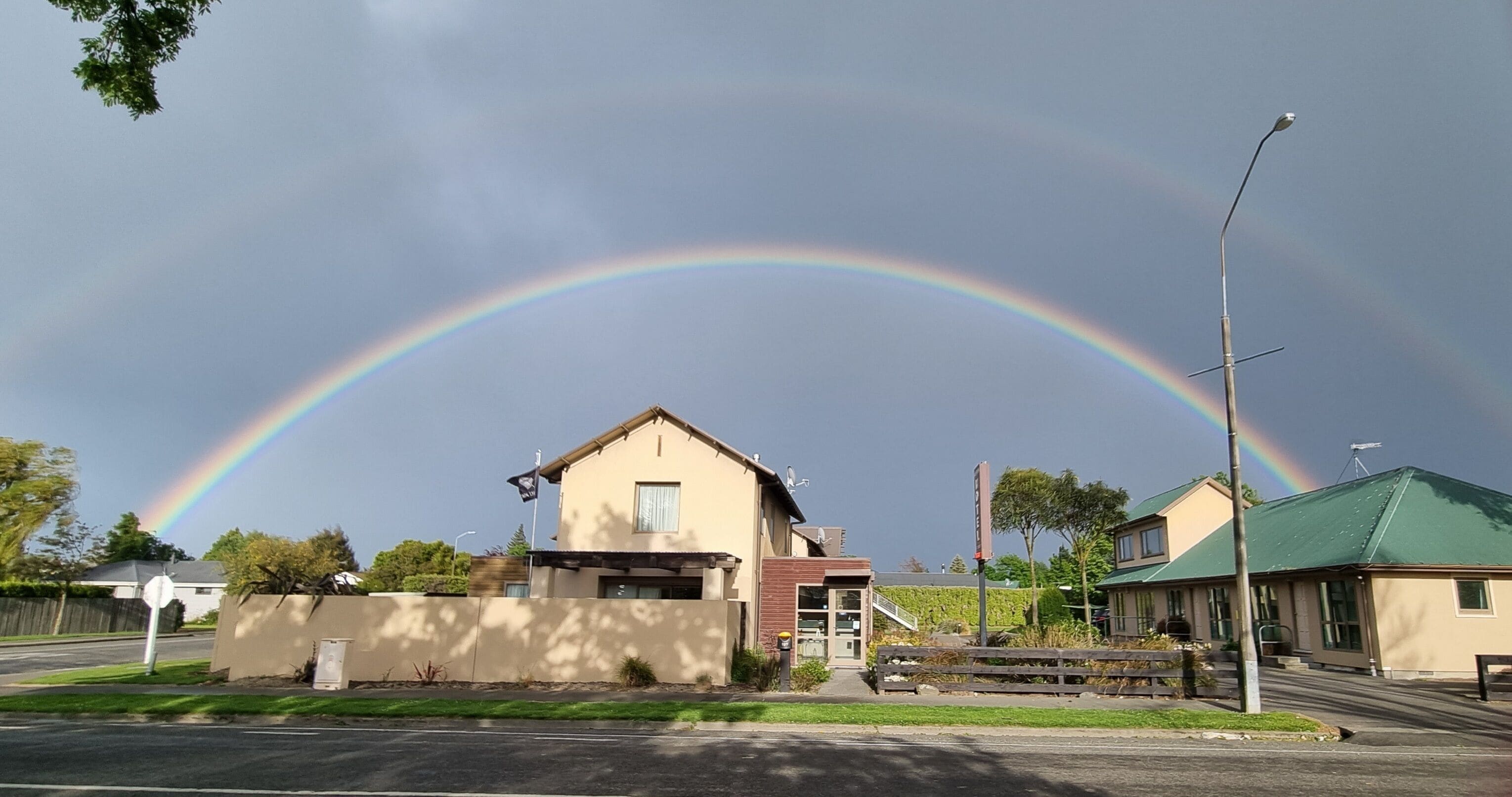 Een woonwijk met een huis, een straat en een regenboog aan de lucht.