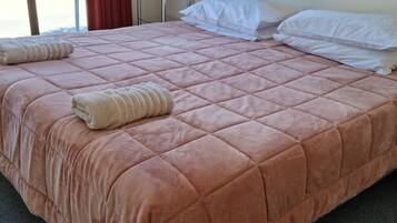 Una cama bien hecha con colcha rosa, almohadas blancas y una toalla doblada.