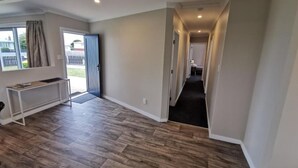 A spacious hallway with wooden flooring, a bench, and a door leading outside.