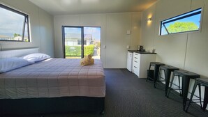 A hotel room with a bed, a desk, a chair, a small kitchenette, and a sliding glass door leading to a balcony.