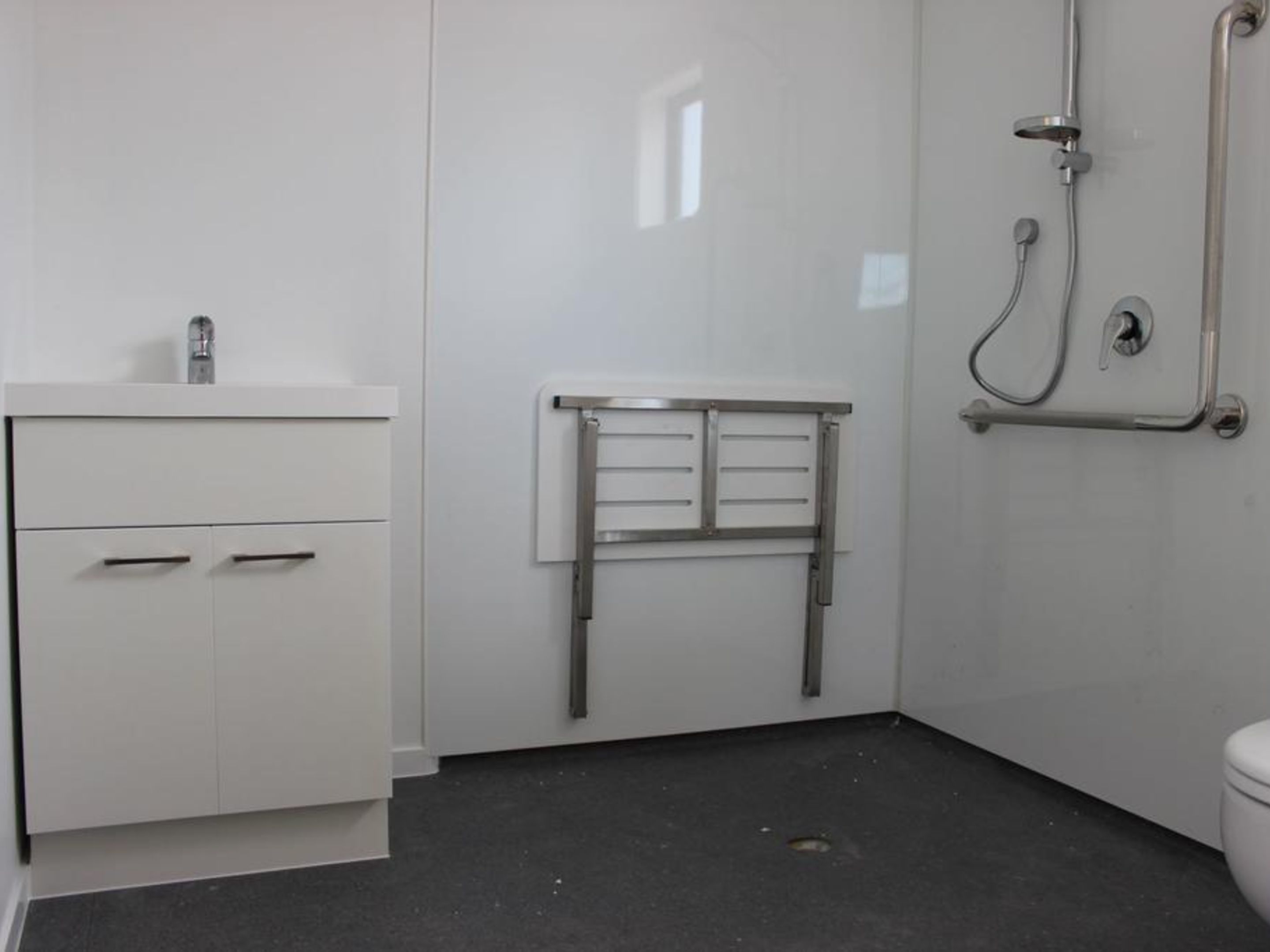 A bathroom with a white sink, a mirror, a towel rack, and a shower with a grab bar.