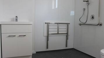 A bathroom with a white sink, a mirror, a towel rack, and a shower with a grab bar.