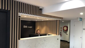Een receptiebalie met een bordje met daarop 'ibis budget', een beveiligingscamera erboven en een bord 'uitgang'.
