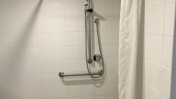 A shower area with a handrail, a showerhead, and a curtain.