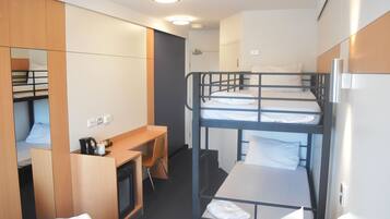 A compact hotel room with bunk beds, a desk, and a small kitchenette.