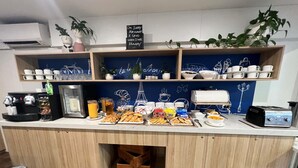 Een ontbijtbuffet met diverse etenswaren, koffieautomaten en een schoolbord met tekst.