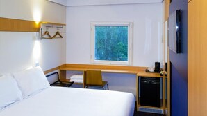 Hotelkamer met een bed, bureau, stoel, kleine televisie, raam met uitzicht op bomen en een wandtelevisie.