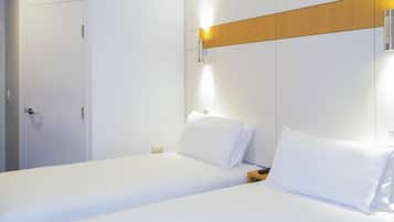A hotel room with two single beds, a wooden panel on the wall, a wall-mounted light, and a door.