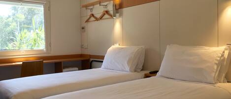 Ett hotellrum med två sängar, ett skrivbord och ett fönster med utsikt över grönområden.