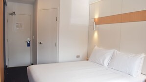 Ein Hotelzimmer mit einem großen Bett, einem Holzkopfteil, einer Tür mit Spiegel und einem kleinen Nachttisch.