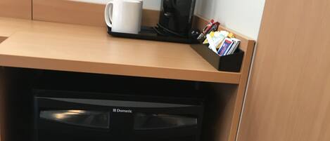 A compact kitchenette with a black refrigerator, a coffee maker, and a white mug on the countertop.