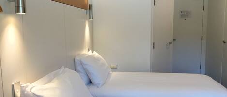 A hotel room with a bed, a wooden headboard, and a wall-mounted light fixture.