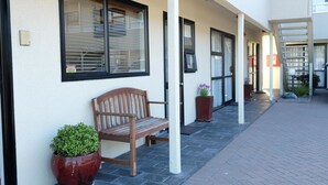 A building exterior with a wooden bench, potted plants, and a staircase leading to an upper level. - Marksman Motor Inn (Wellington)