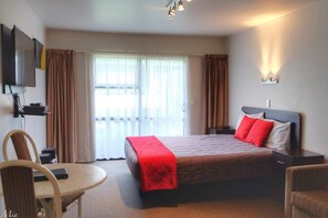 A hotel room with a bed, a desk, a chair, a TV, and a window with curtains.