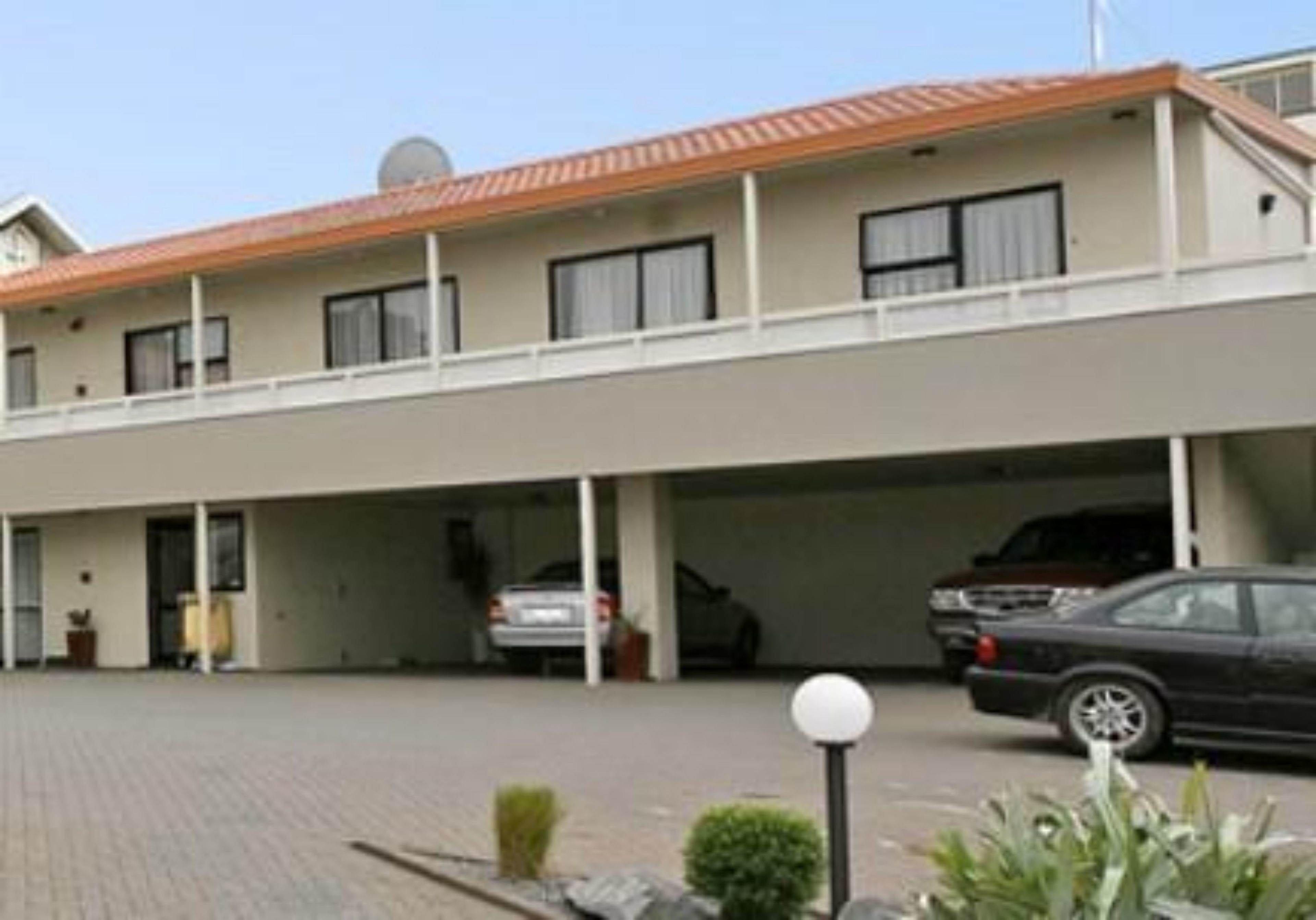 Un edificio a due piani con tetto piatto, un'area di parcheggio coperta e un'auto parcheggiata all'interno.