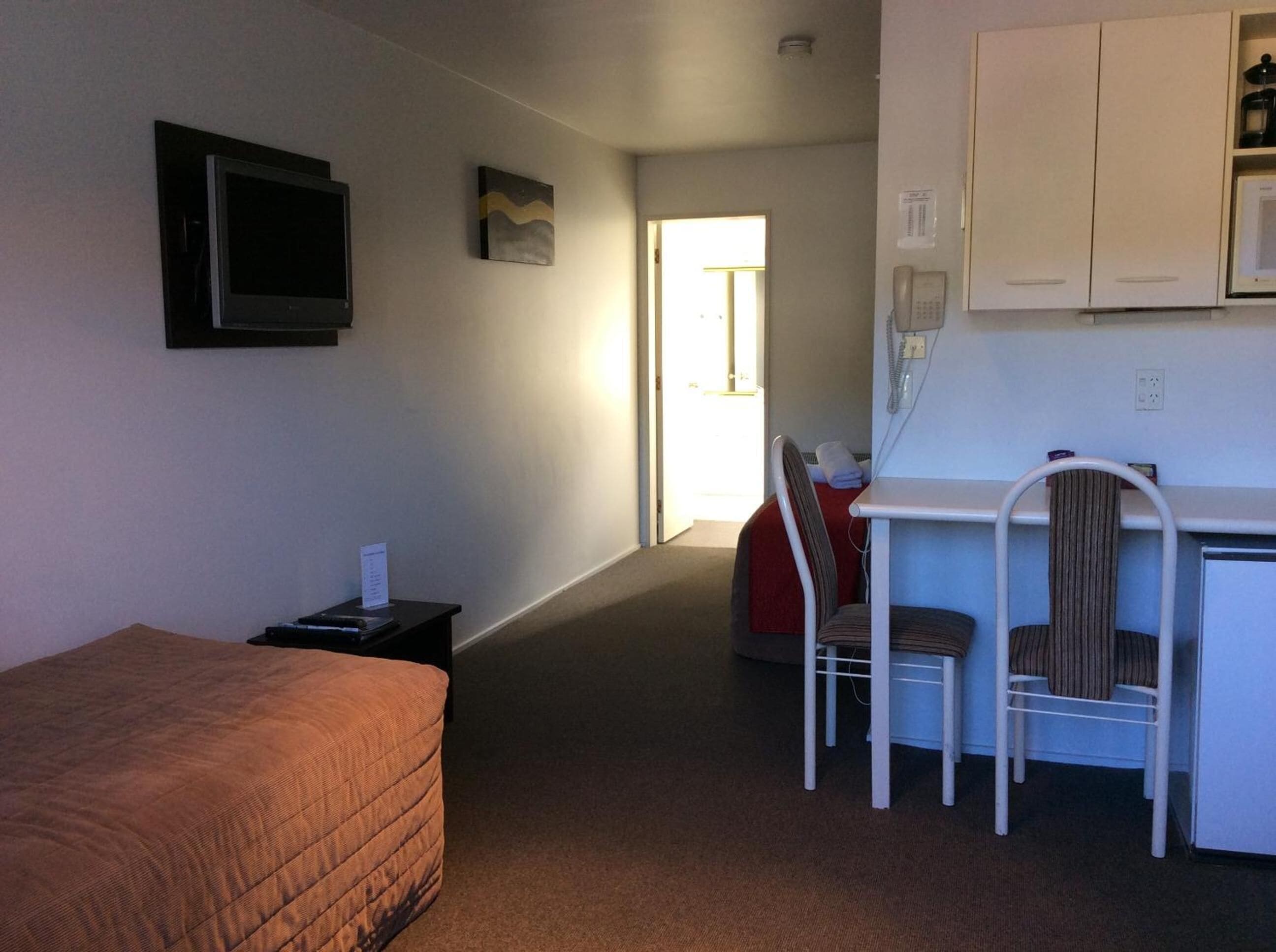 A compact room with a bed, a desk, a chair, and a kitchenette.