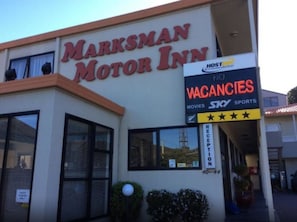 Het uiterlijk van Marksman Motor Inn, met een bord waarop staat 'geen kamers beschikbaar' en voorzieningen zoals films en sport.