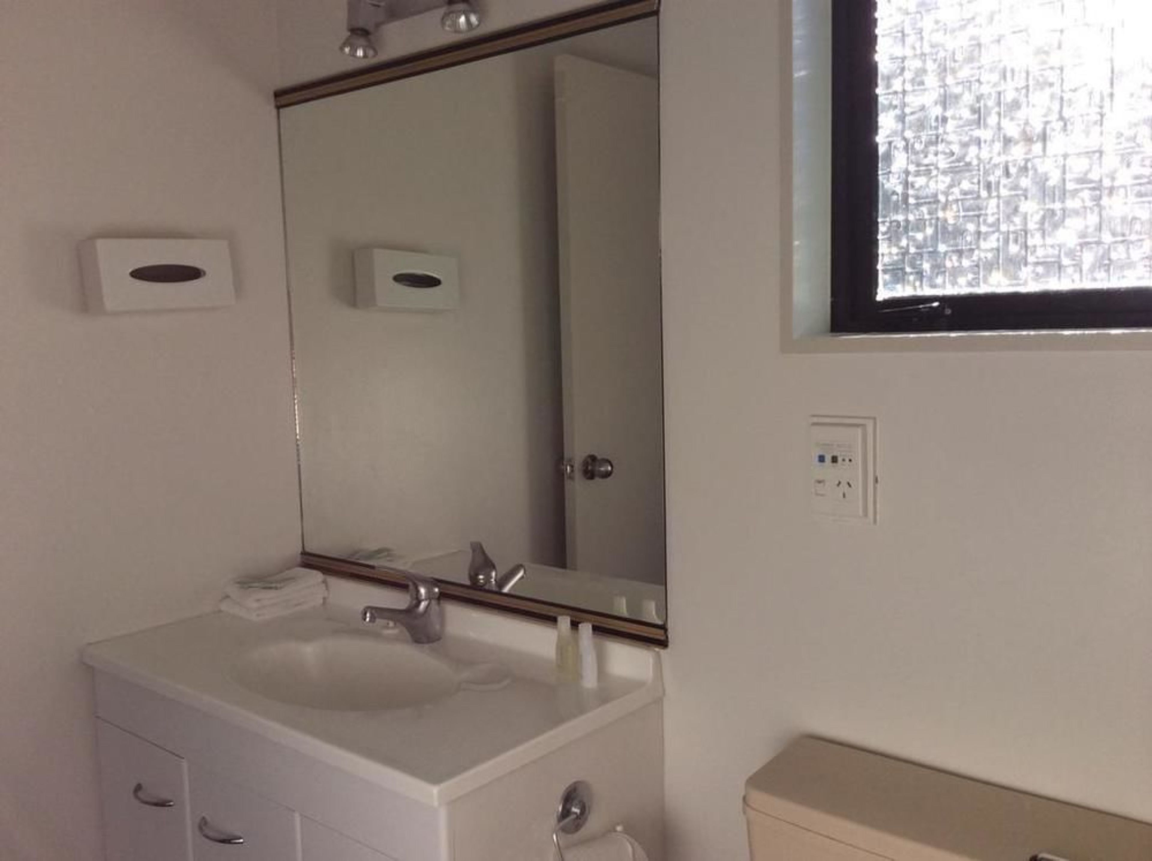 A bathroom with a white sink, a mirror, a toilet, and a window with a view of a building.