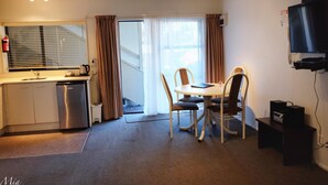 A compact kitchen with a dishwasher, a dining table with four chairs, a television, and a fire extinguisher. - Marksman Motor Inn (Wellington)
